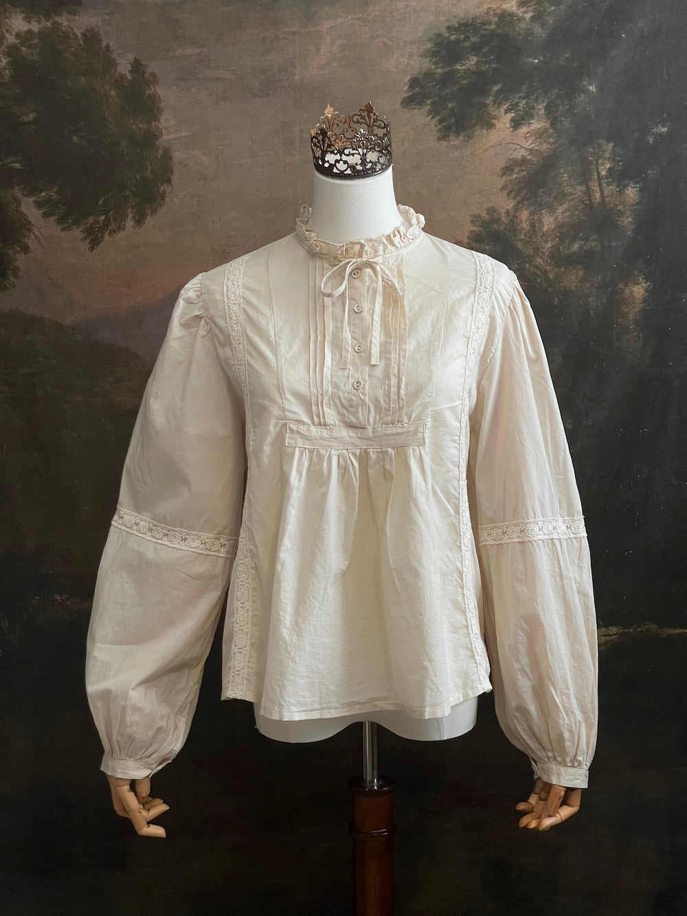 A historically inspired regency and victorian style high neck beige cotton blouse with bishop sleeves and lace trim on a mannequin