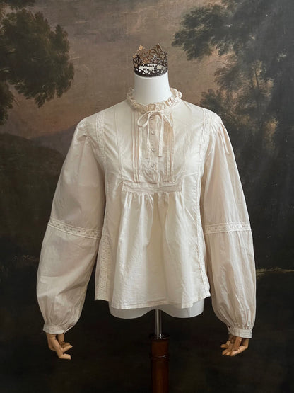 A historically inspired regency and victorian style high neck beige cotton blouse with bishop sleeves and lace trim on a mannequin