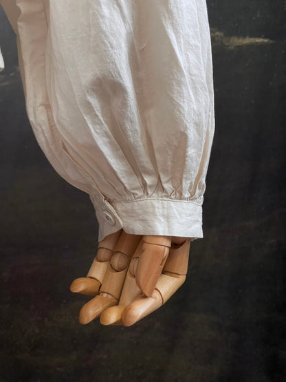 A historically inspired regency and victorian style high neck beige cotton blouse with bishop sleeves and lace trim on a mannequin