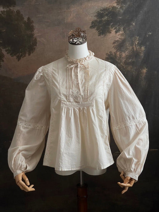A historically inspired regency and victorian style high neck beige cotton blouse with bishop sleeves and lace trim on a mannequin