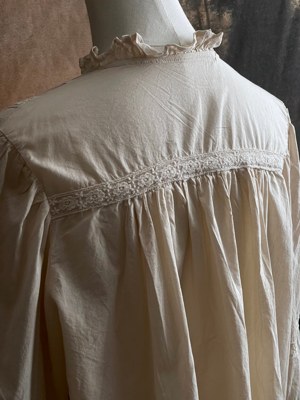 A historically inspired regency and victorian style high neck beige cotton blouse with bishop sleeves and lace trim on a mannequin