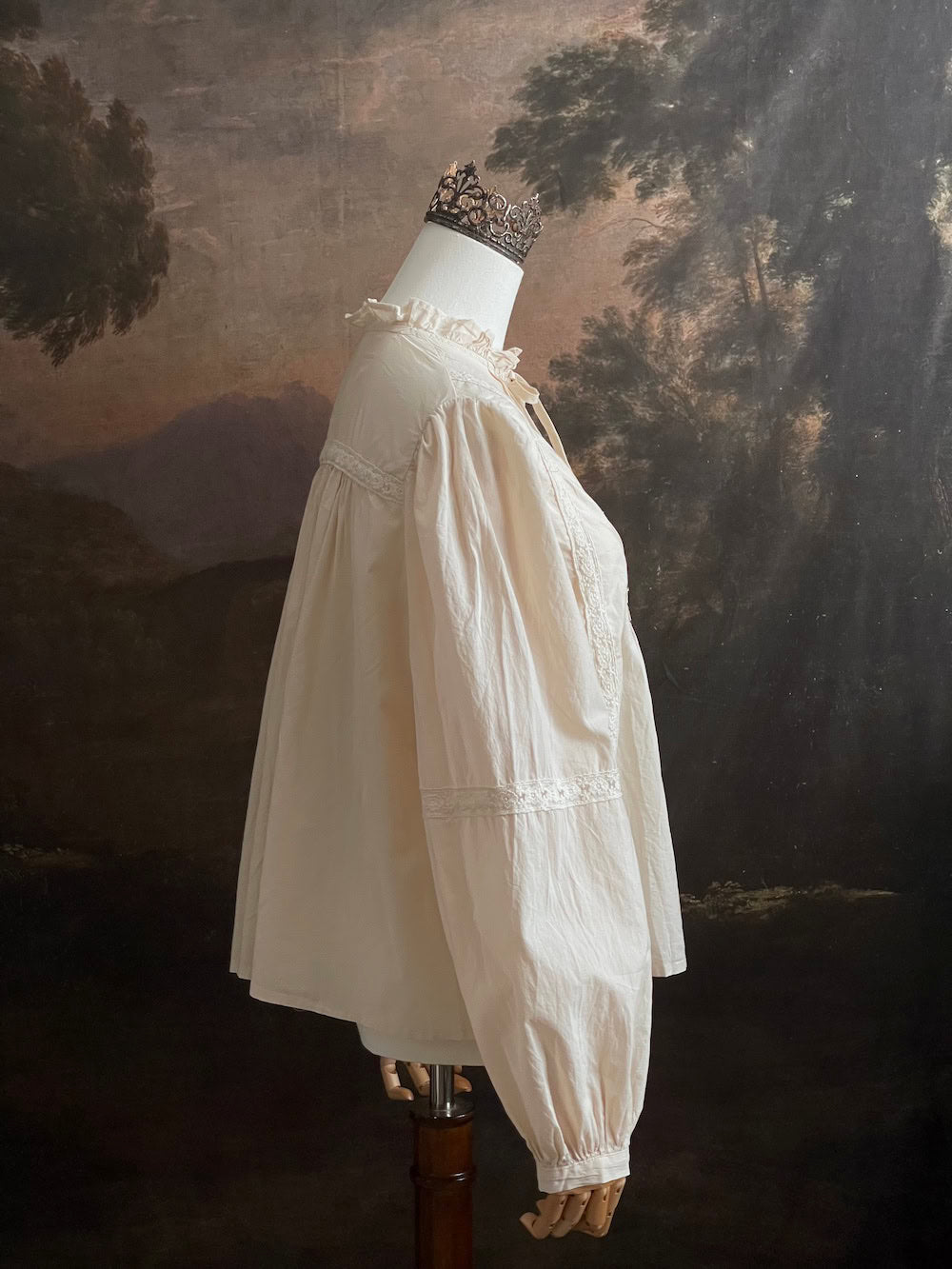 A historically inspired regency and victorian style high neck beige cotton blouse with bishop sleeves and lace trim on a mannequin