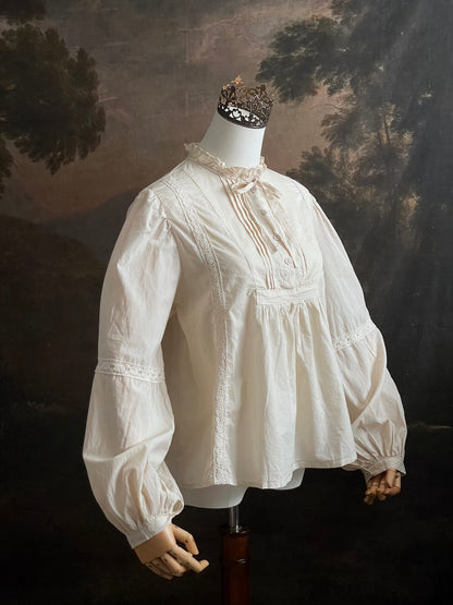 A historically inspired regency and victorian style high neck beige cotton blouse with bishop sleeves and lace trim on a mannequin