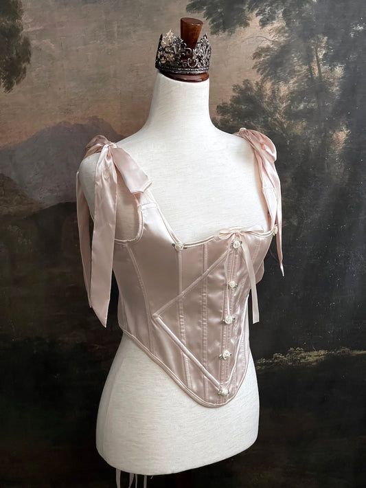 A historical fashion inspired rococo and baroque era champagne satin corset stays with bow straps and rosette applique on a mannequin