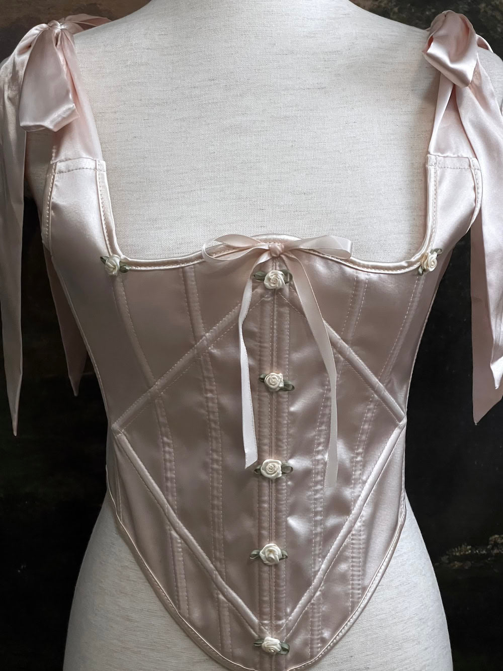 A historical fashion inspired rococo and baroque era champagne satin corset stays with bow straps and rosette applique on a mannequin