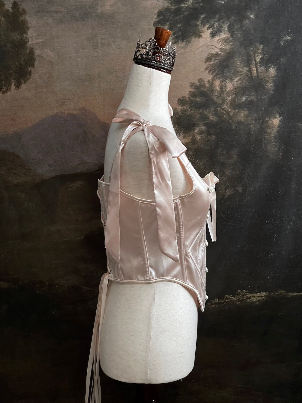 A historical fashion inspired rococo and baroque era champagne satin corset stays with bow straps and rosette applique on a mannequin