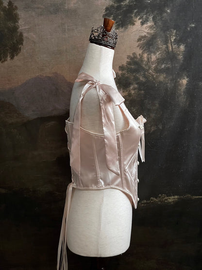 A historical fashion inspired rococo and baroque era champagne satin corset stays with bow straps and rosette applique on a mannequin