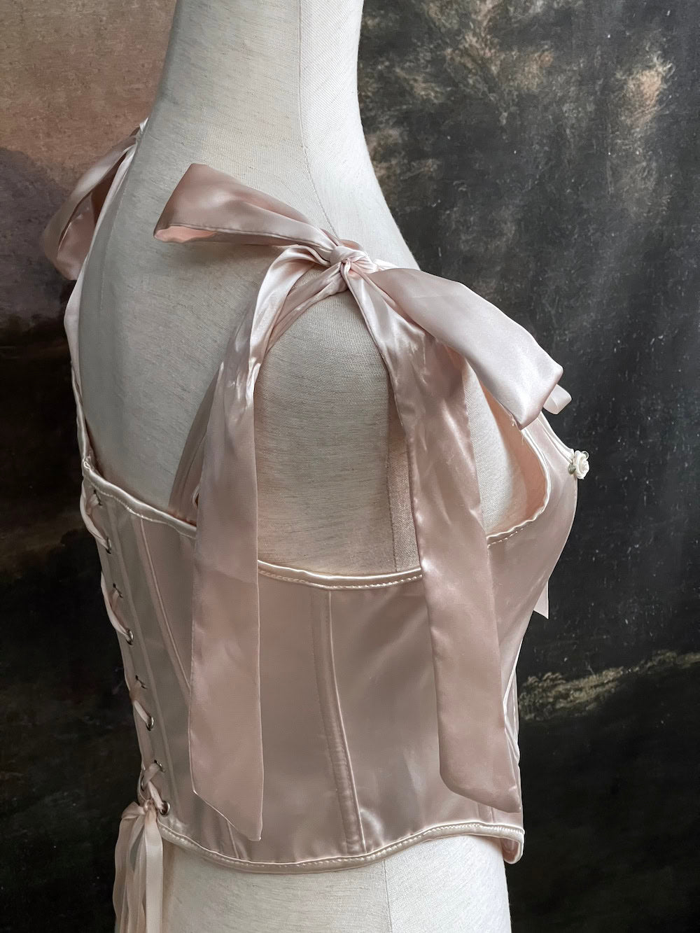 A historical fashion inspired rococo and baroque era champagne satin corset stays with bow straps and rosette applique on a mannequin