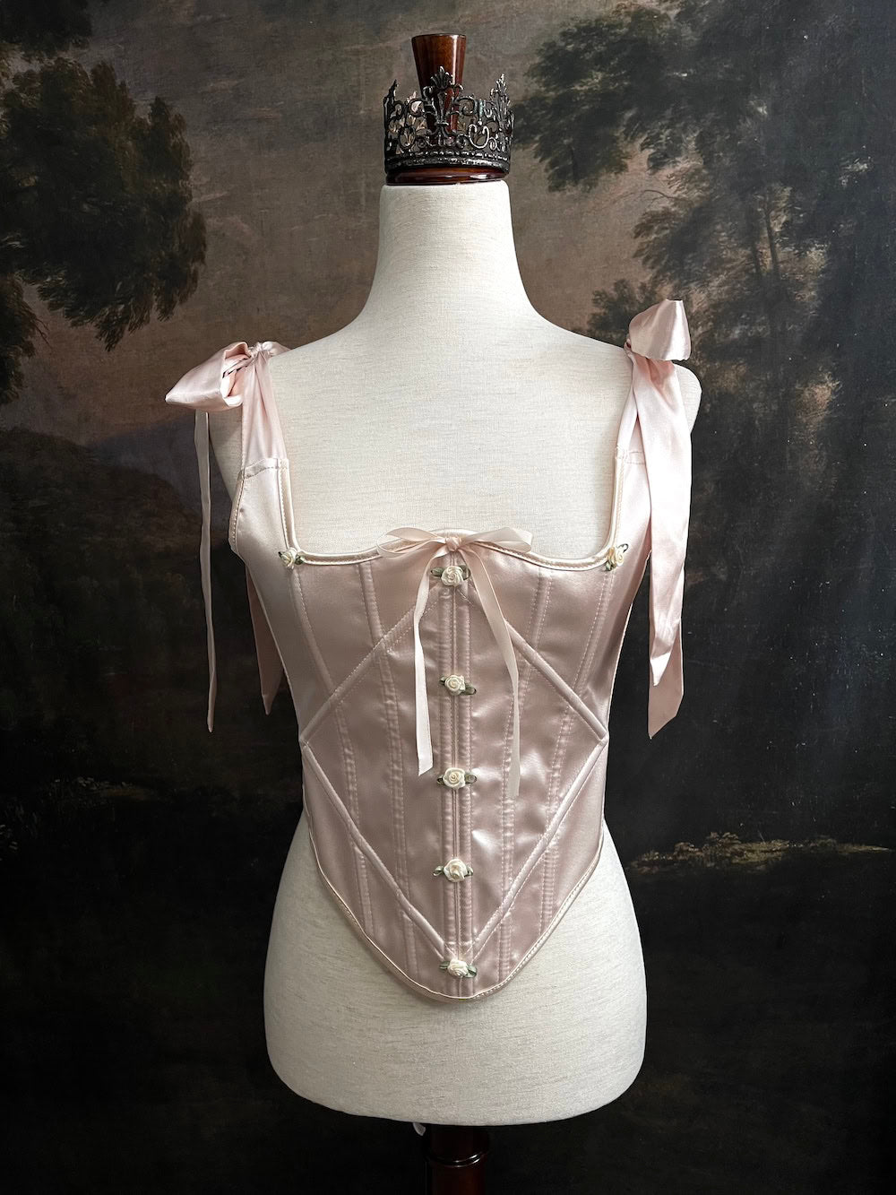 A historical fashion inspired rococo and baroque era champagne satin corset stays with bow straps and rosette applique on a mannequin