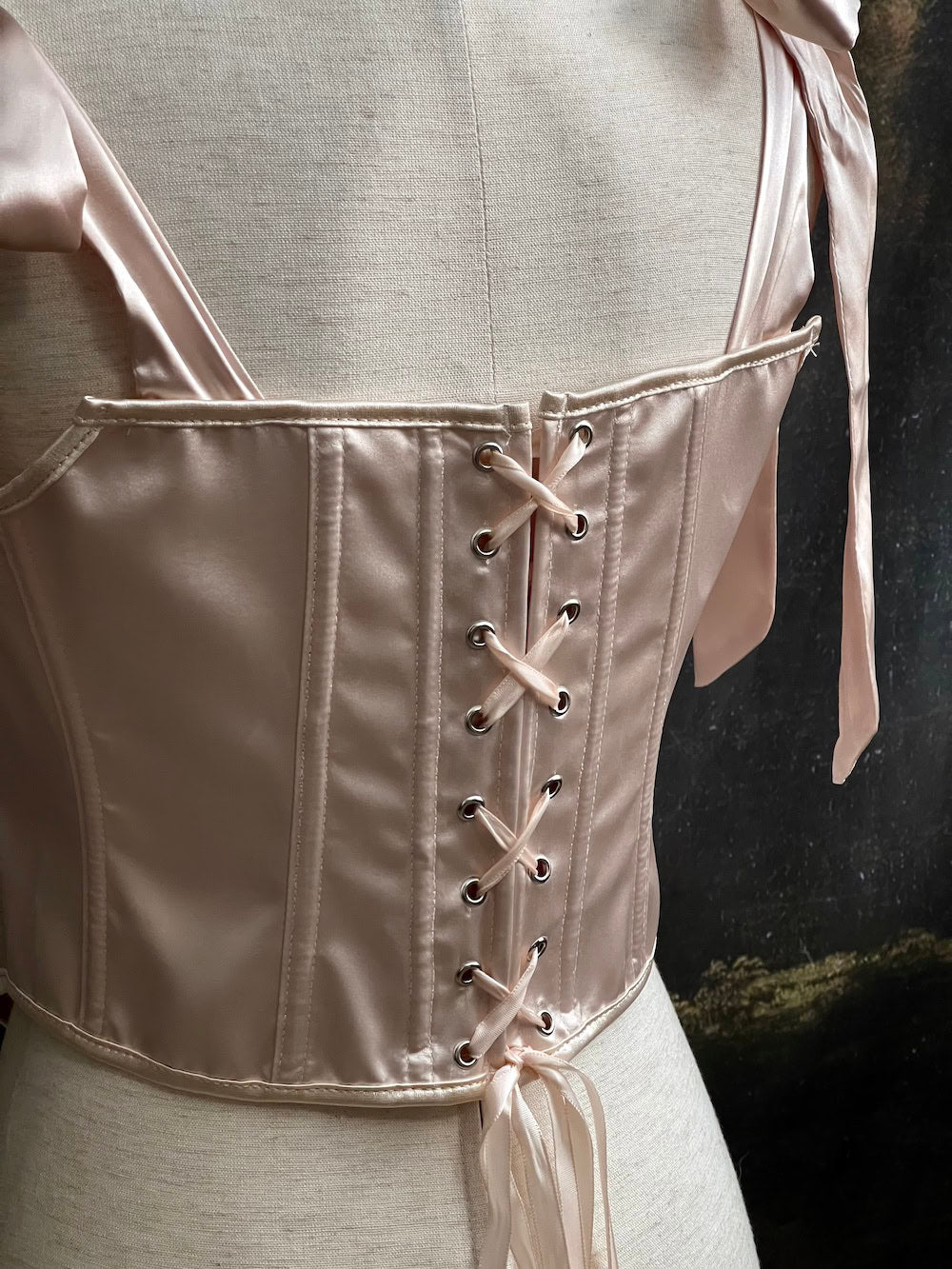 A historical fashion inspired rococo and baroque era champagne satin corset stays with bow straps and rosette applique on a mannequin