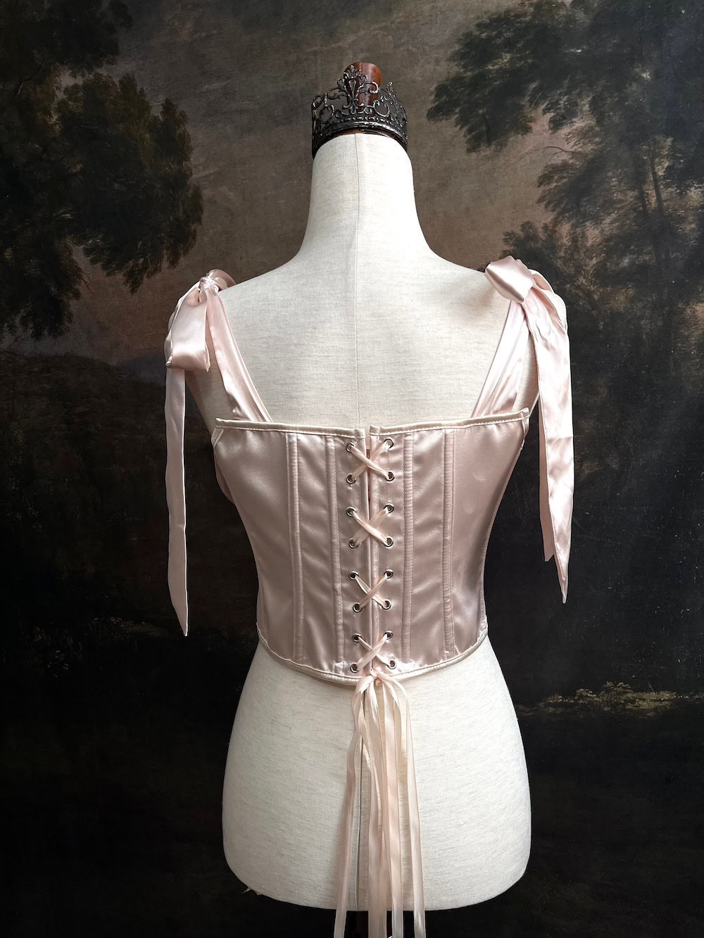 A historical fashion inspired rococo and baroque era champagne satin corset stays with bow straps and rosette applique on a mannequin