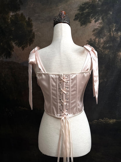 A historical fashion inspired rococo and baroque era champagne satin corset stays with bow straps and rosette applique on a mannequin