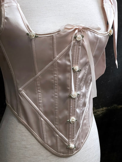A historical fashion inspired rococo and baroque era champagne satin corset stays with bow straps and rosette applique on a mannequin