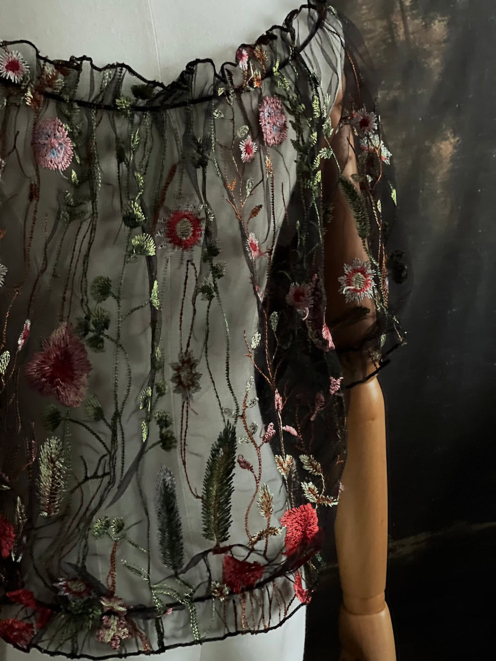 details of a gothic black sheer mesh puff sleeve blouse with embroidered botanicals and a ruffle hem, on a forest-themed art history background