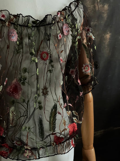 details of a gothic black sheer mesh puff sleeve blouse with embroidered botanicals and a ruffle hem, on a forest-themed art history background