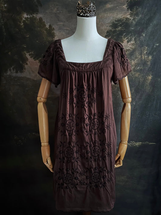 A Vintage Y2K Bohemian Boho Brown Cotton Tunic Dress with Ornate Fleur Embroidery and short scalloped sleeves on a mannequin in front of an art history backdrop
