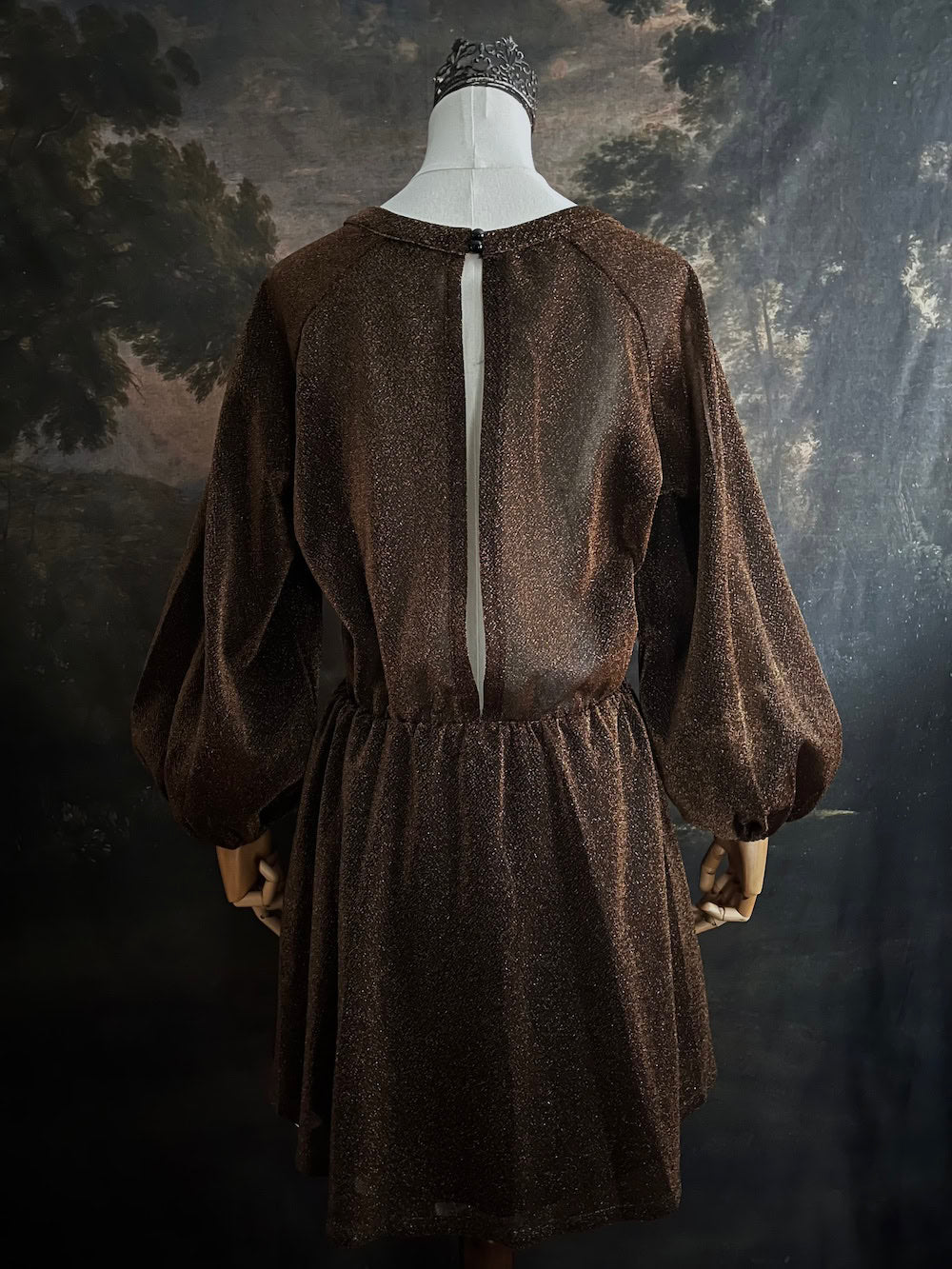 A medieval knight inspired metallic brown / bronze tunic dress with puffy bishop sleeves on a mannequin in front of an art history backdrop