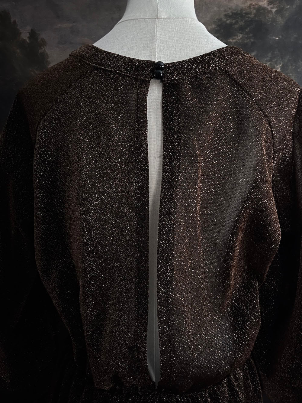 A medieval knight inspired metallic brown / bronze tunic dress with puffy bishop sleeves on a mannequin in front of an art history backdrop
