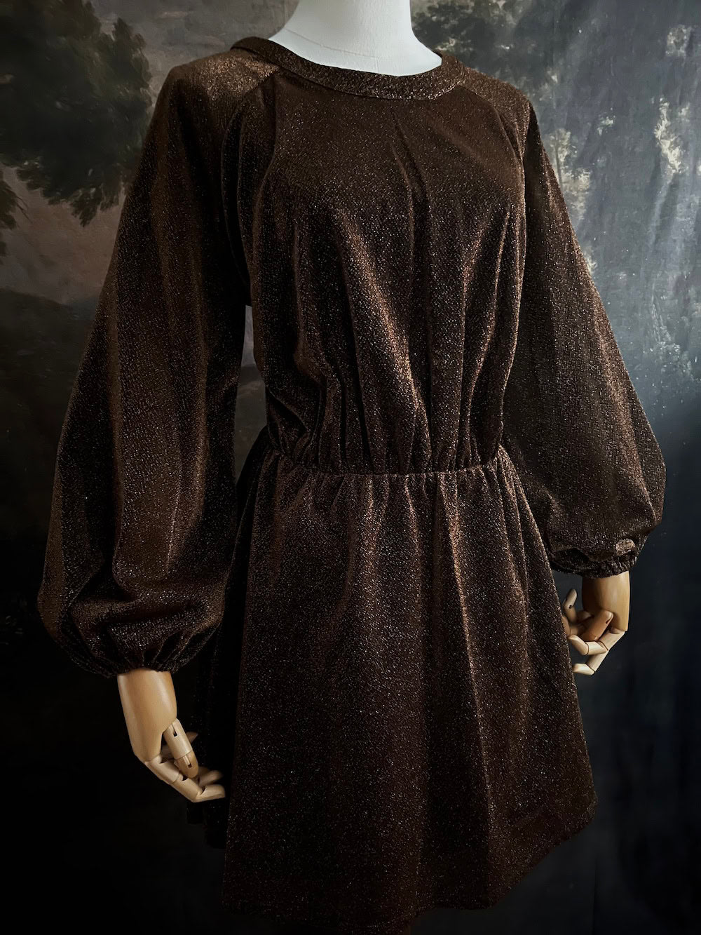 A medieval knight inspired metallic brown / bronze tunic dress with puffy bishop sleeves on a mannequin in front of an art history backdrop