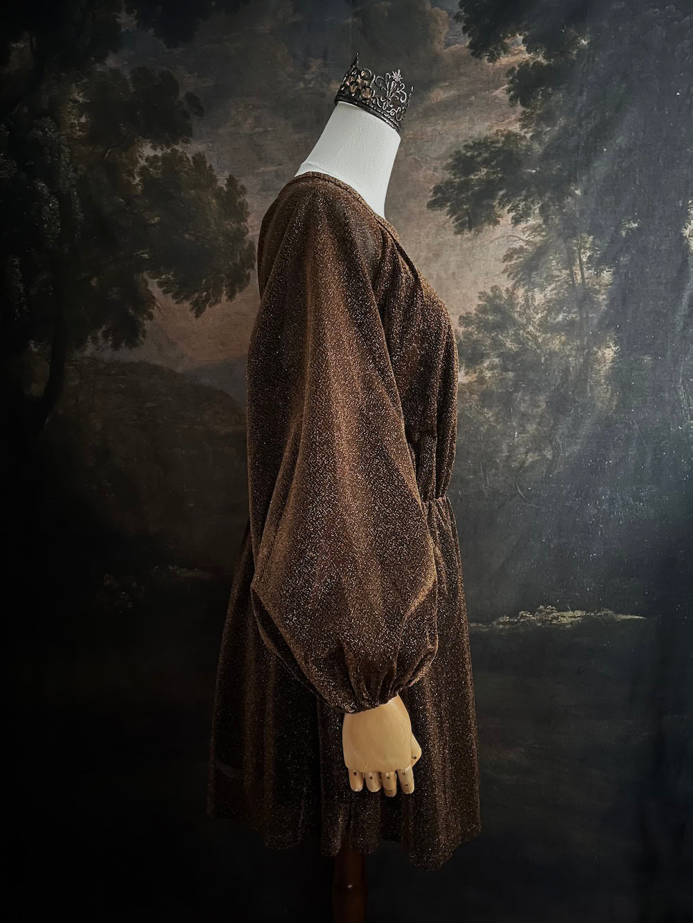 A medieval knight inspired metallic brown / bronze tunic dress with puffy bishop sleeves on a mannequin in front of an art history backdrop