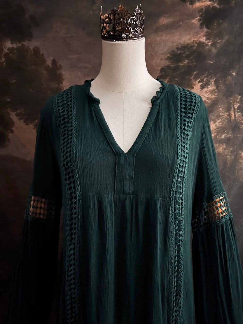 A historical fantasy inspired dark green bohemian medieval revival style dress on a mannequin in front of an art history backdrop