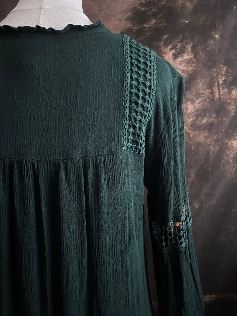 A historical fantasy inspired dark green bohemian medieval revival style dress on a mannequin in front of an art history backdrop