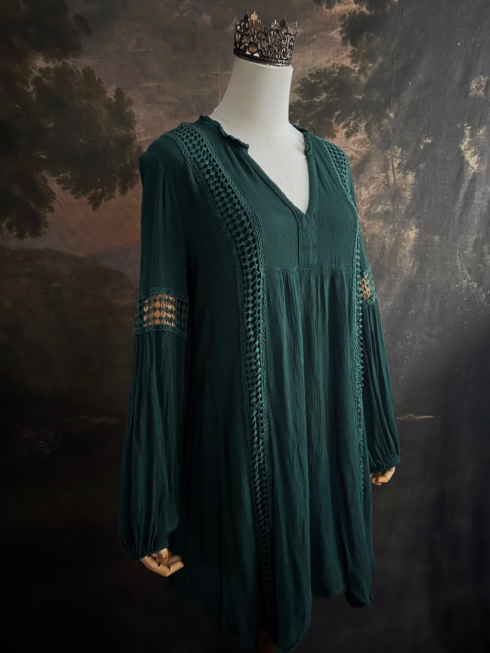 A historical fantasy inspired dark green bohemian medieval revival style dress on a mannequin in front of an art history backdrop