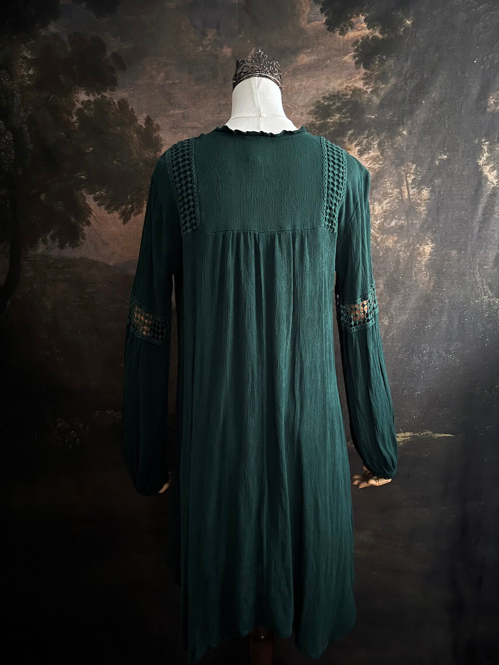 A historical fantasy inspired dark green bohemian medieval revival style dress on a mannequin in front of an art history backdrop