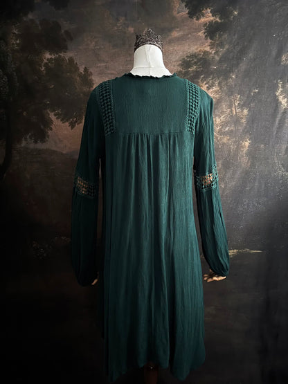 A historical fantasy inspired dark green bohemian medieval revival style dress on a mannequin in front of an art history backdrop