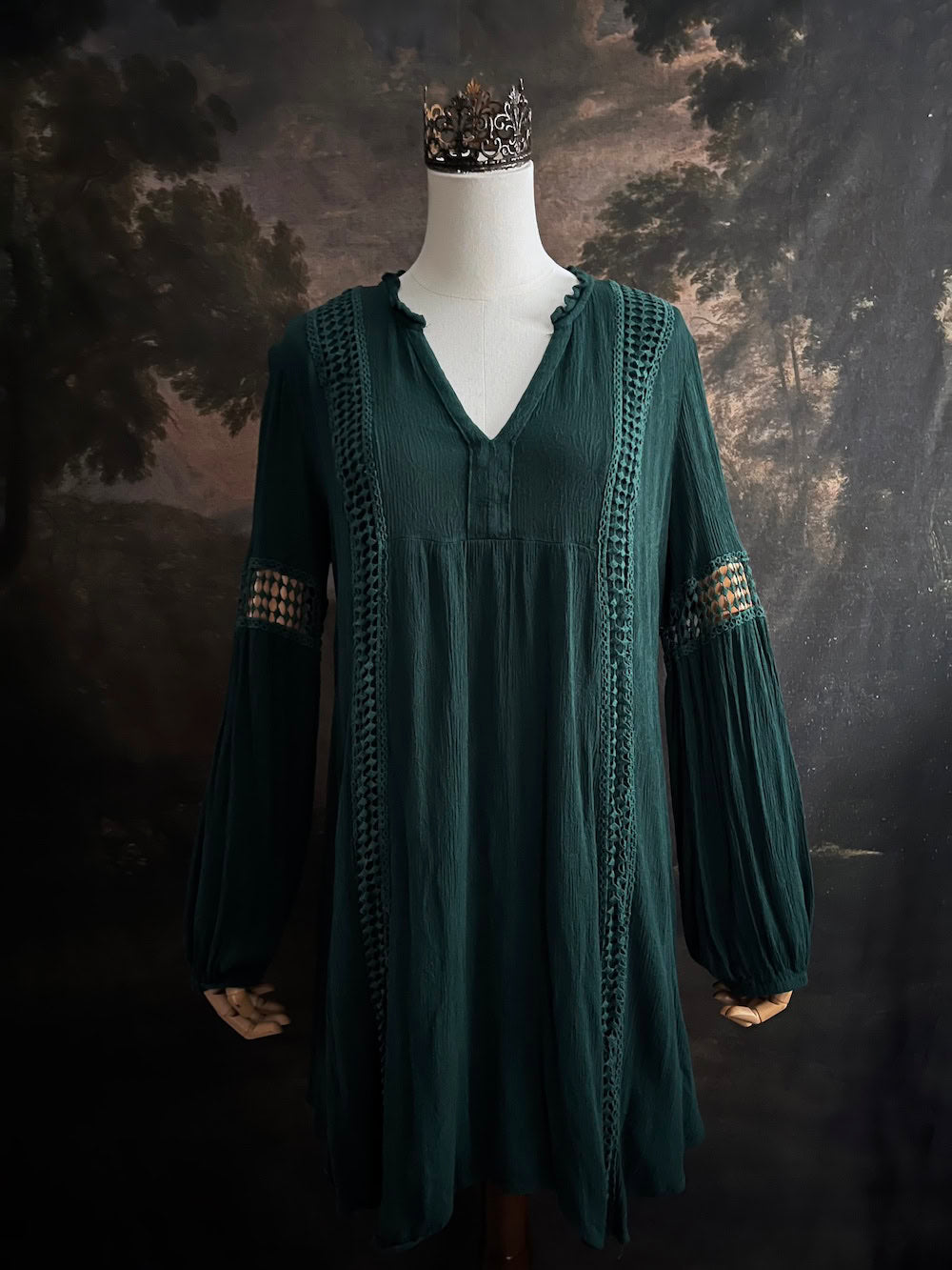 A historical fantasy inspired dark green bohemian medieval revival style dress on a mannequin in front of an art history backdrop