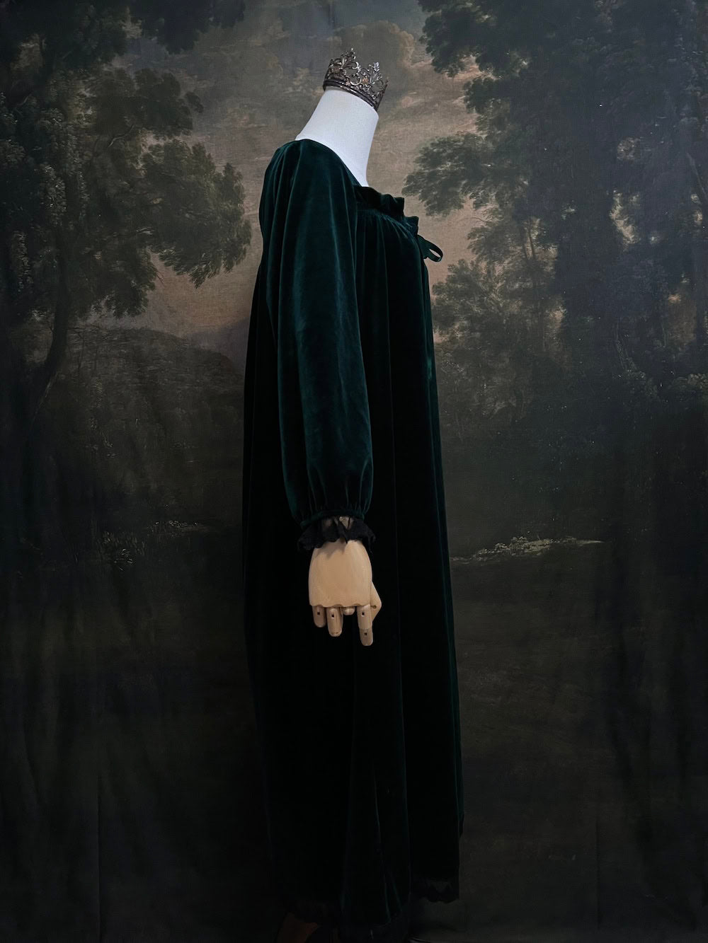 A dark forest emerald green velour velvet square neckline long sleeve midi dress with black floral lace trim and a satin drawstring on an art history backdrop