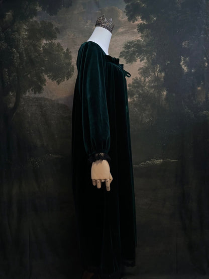 A dark forest emerald green velour velvet square neckline long sleeve midi dress with black floral lace trim and a satin drawstring on an art history backdrop