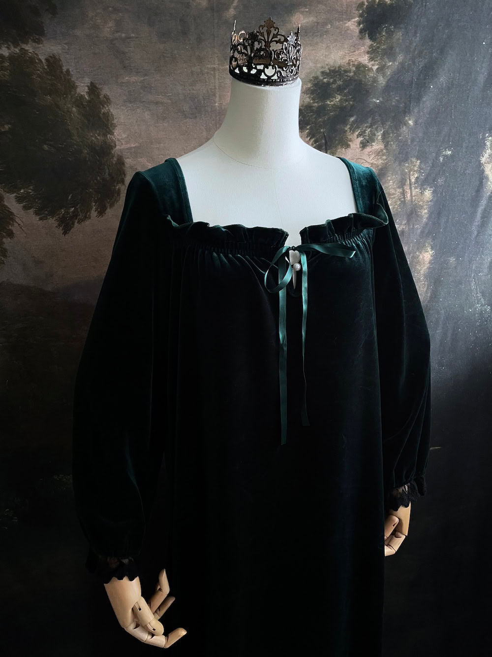 A dark forest emerald green velour velvet square neckline long sleeve midi dress with black floral lace trim and a satin drawstring on an art history backdrop