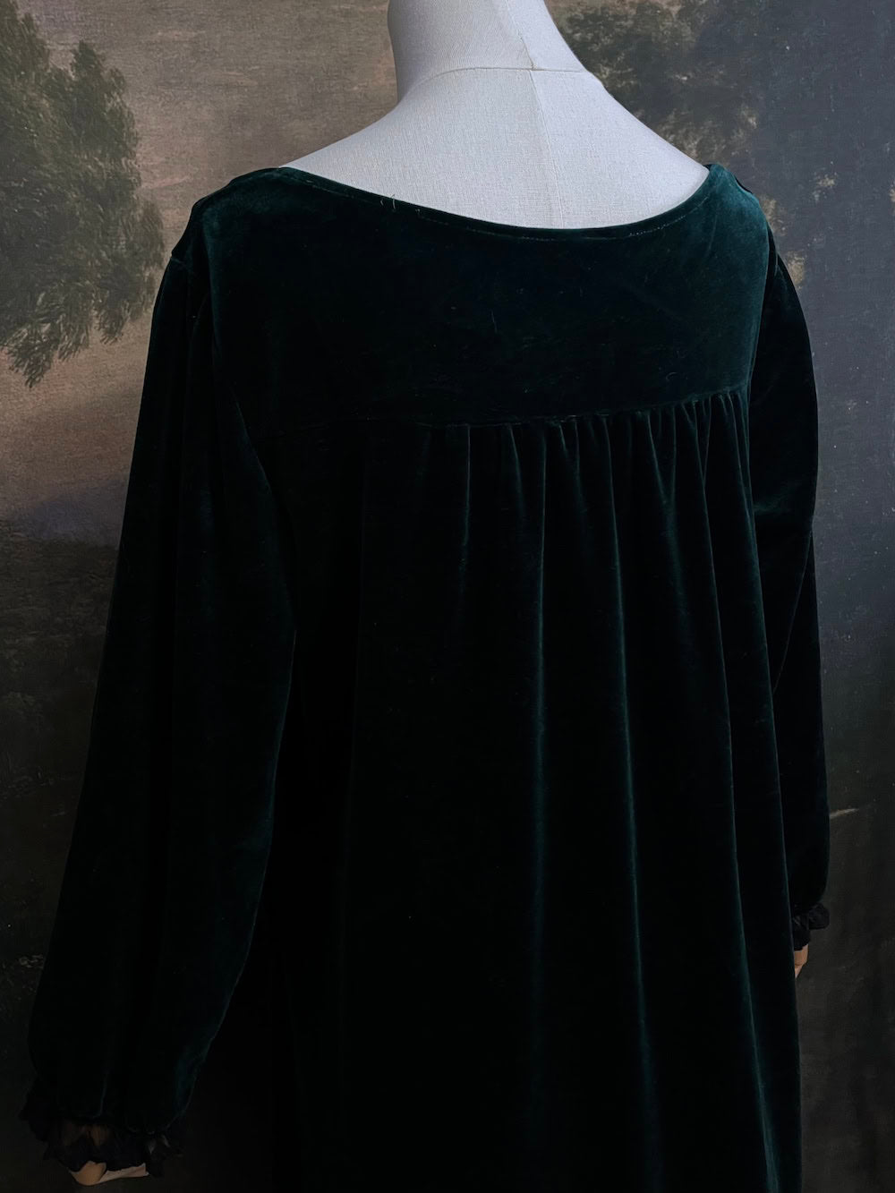 A dark forest emerald green velour velvet square neckline long sleeve midi dress with black floral lace trim and a satin drawstring on an art history backdrop