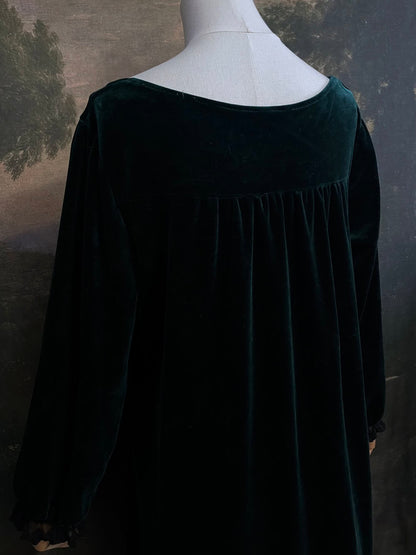 A dark forest emerald green velour velvet square neckline long sleeve midi dress with black floral lace trim and a satin drawstring on an art history backdrop