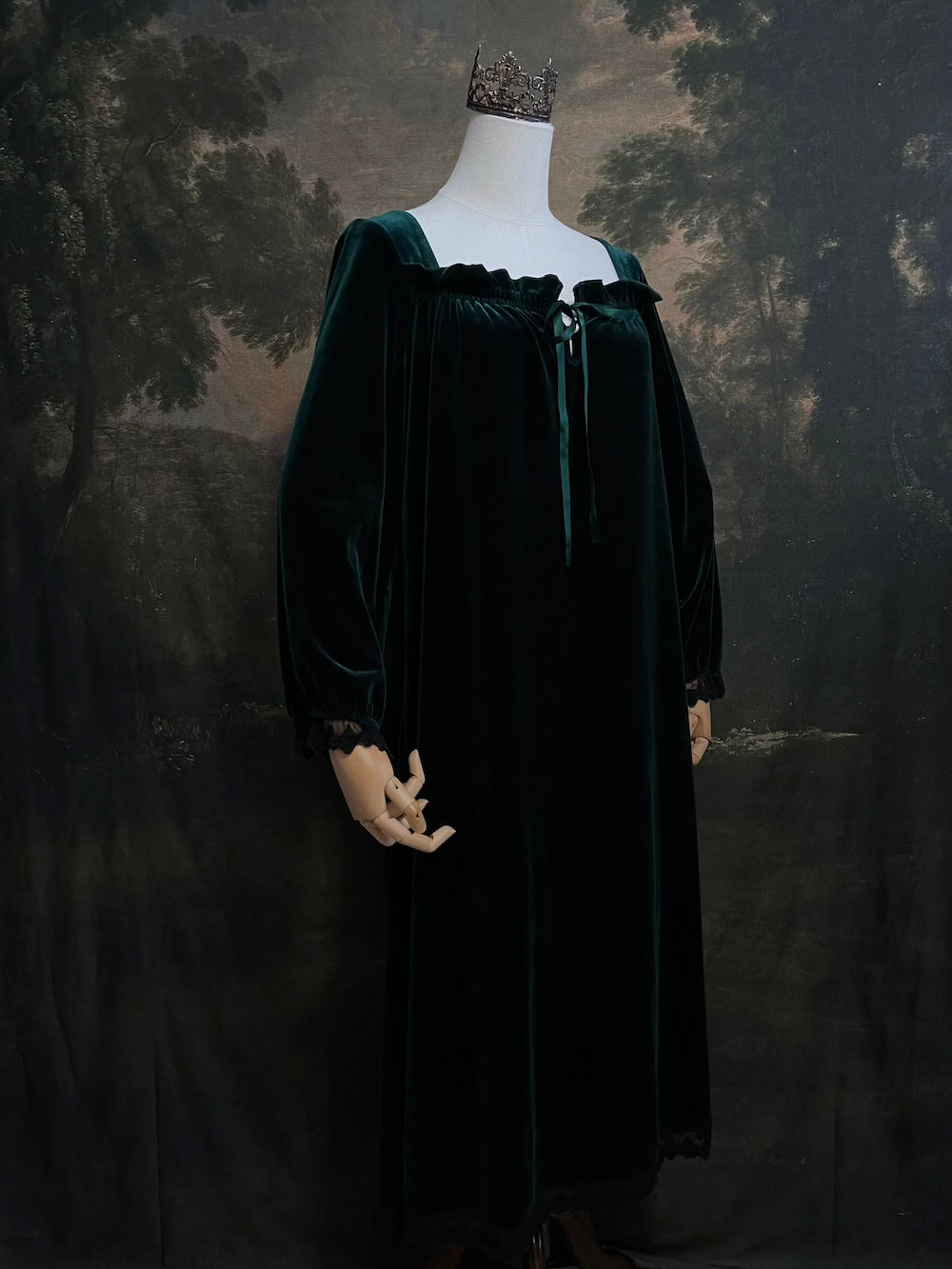 A dark forest emerald green velour velvet square neckline long sleeve midi dress with black floral lace trim and a satin drawstring on an art history backdrop