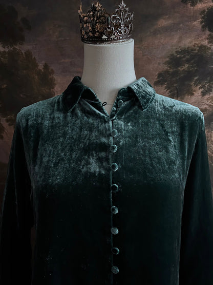 Mannequin wearing a dark green velvet button up vintage medieval revival style collared shirt against a dark, forest-themed art history background