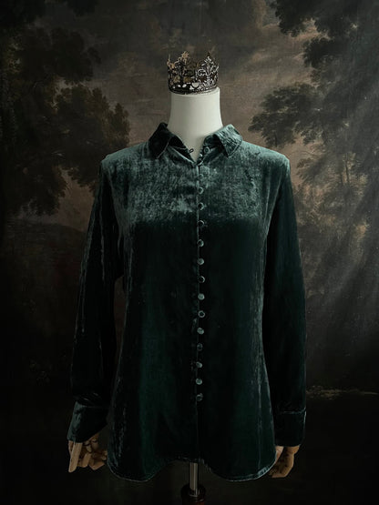 Mannequin wearing a dark green velvet button up vintage medieval revival style collared shirt against a dark, forest-themed art history background