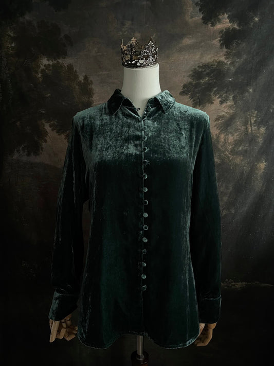 Mannequin wearing a dark green velvet button up vintage medieval revival style collared shirt against a dark, forest-themed art history background