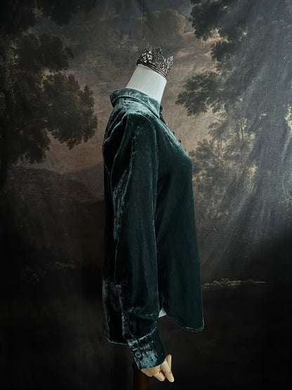 Mannequin wearing a dark green velvet button up vintage medieval revival style collared shirt against a dark, forest-themed art history background