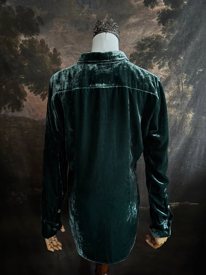 Mannequin wearing a dark green velvet button up vintage medieval revival style collared shirt against a dark, forest-themed art history background