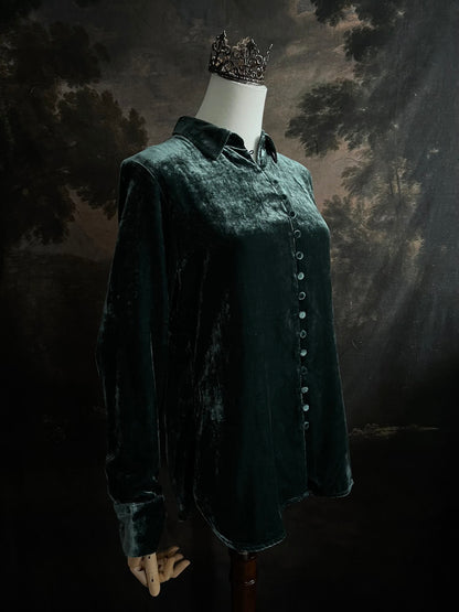 Mannequin wearing a dark green velvet button up vintage medieval revival style collared shirt against a dark, forest-themed art history background