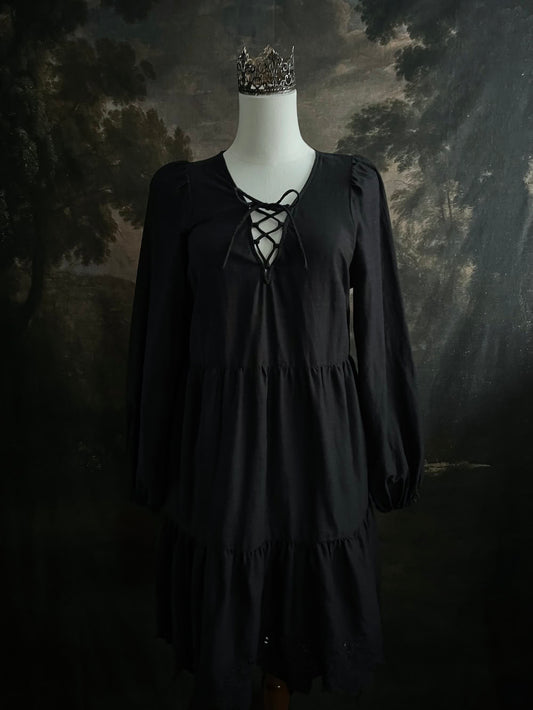 Historically inspired witchy gothic black tiered mini dress with corset lace up bodice and long bishop sleeves on a mannequin in front of a dark art history backdrop