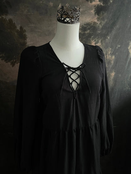 Historically inspired witchy gothic black tiered mini dress with corset lace up bodice and long bishop sleeves on a mannequin in front of a dark art history backdrop