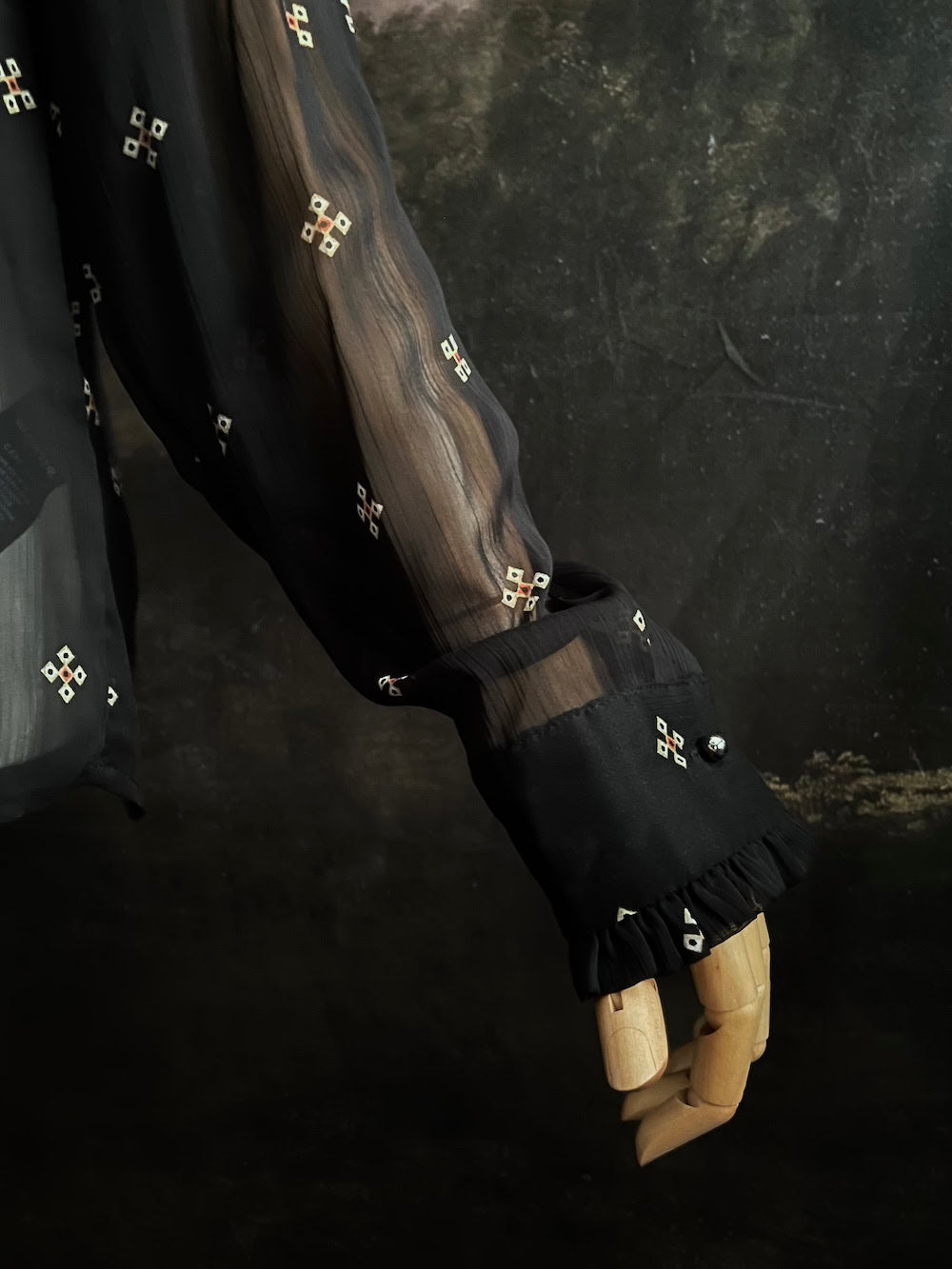 Mannequin wearing a historically-inspired yoked mock neck black blouse with cross patterns against a dark, forested painting background.