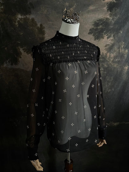 Mannequin wearing a historically-inspired yoked mock neck black blouse with cross patterns against a dark, forested painting background.