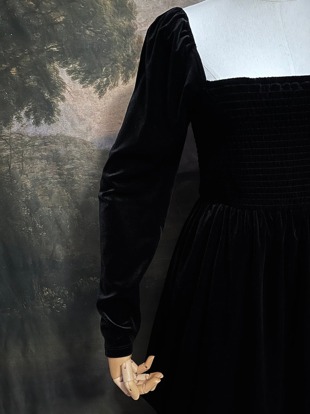 A Black Velvet Shirred Bodice Mini Dress inspired by the tudor and renaissance era on a mannequin in front of an art history backdrop