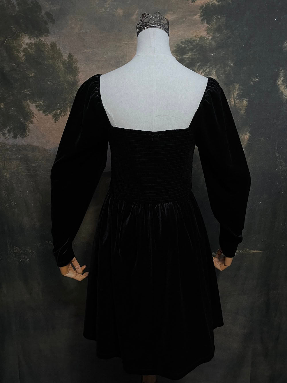 A Black Velvet Shirred Bodice Mini Dress inspired by the tudor and renaissance era on a mannequin in front of an art history backdrop