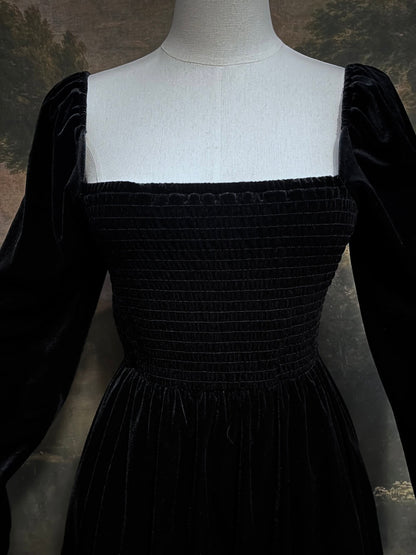 A Black Velvet Shirred Bodice Mini Dress inspired by the tudor and renaissance era on a mannequin in front of an art history backdrop
