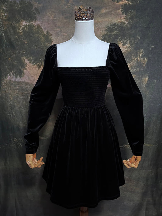 A Black Velvet Shirred Bodice Mini Dress inspired by the tudor and renaissance era on a mannequin in front of an art history backdrop